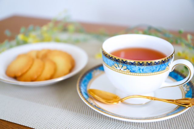 白い編み目のランチョンマットの上に置かれた紅茶とビスケットの皿。ゆったりとしたティータイムの様子は、時間制限食や断続的カロリー制限における「食事の時間帯の選び方」が健康に与える影響を考えるうえで、現代人の日常生活との調和を感じさせる。