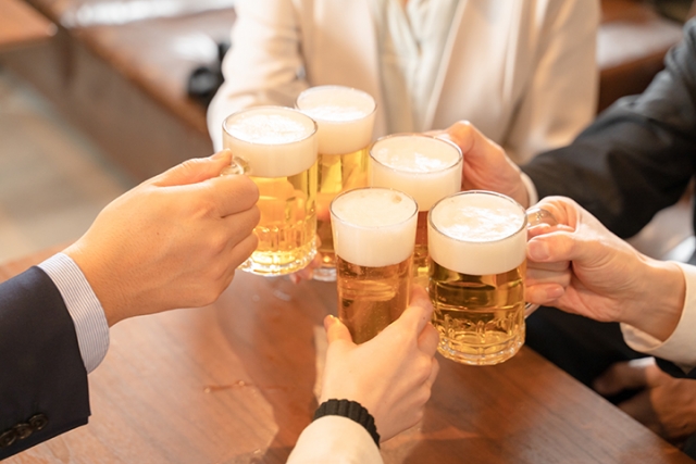 仕事終わりに居酒屋でビールジョッキを乾杯する日本人の手元。泡立つ黄金色のビールが、日本の飲酒文化や日常的な飲み会習慣を象徴している光景