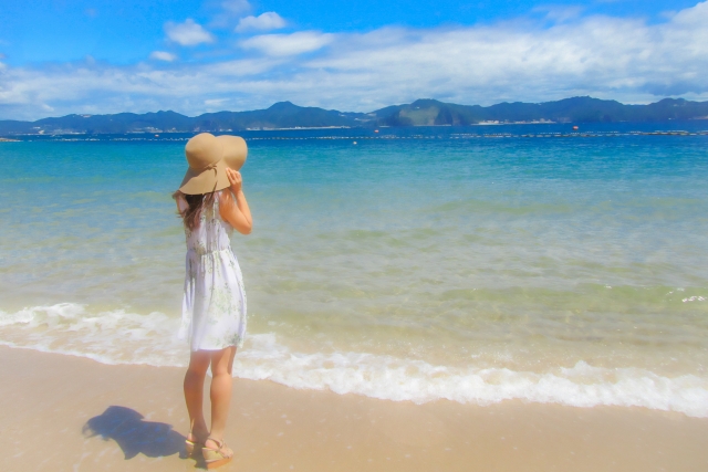 海辺で日焼けした女性が立っている様子。メラニンによる肌の褐色化と、食生活による自然な肌色の変化（カロテノイドによる黄み）との違いを考えるビジュアルとして、外見と健康の関係をテーマにしたコラム記事に関連するイメージ。