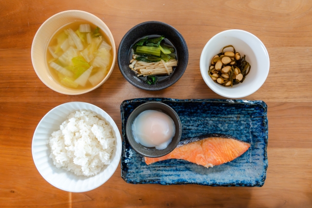 栄養バランスの取れた和食の一汁三菜：ご飯、味噌汁、漬物、豆類、焼き鮭、生卵を含む伝統的な食事例。最適栄養食のモデルとして、内臓脂肪の減少や腸内環境の改善など、科学的に裏付けられた健康効果が注目されている。