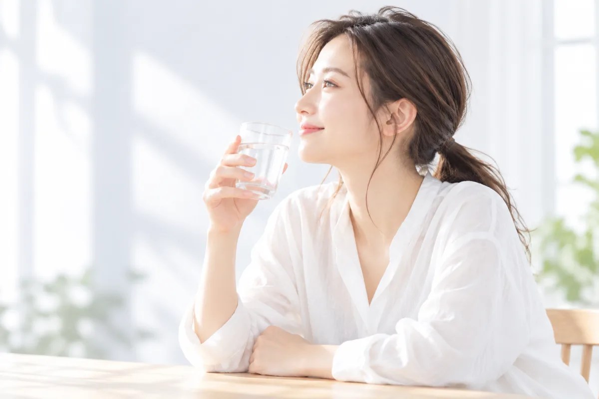 朝、水の入ったコップを手にほほえむ女性