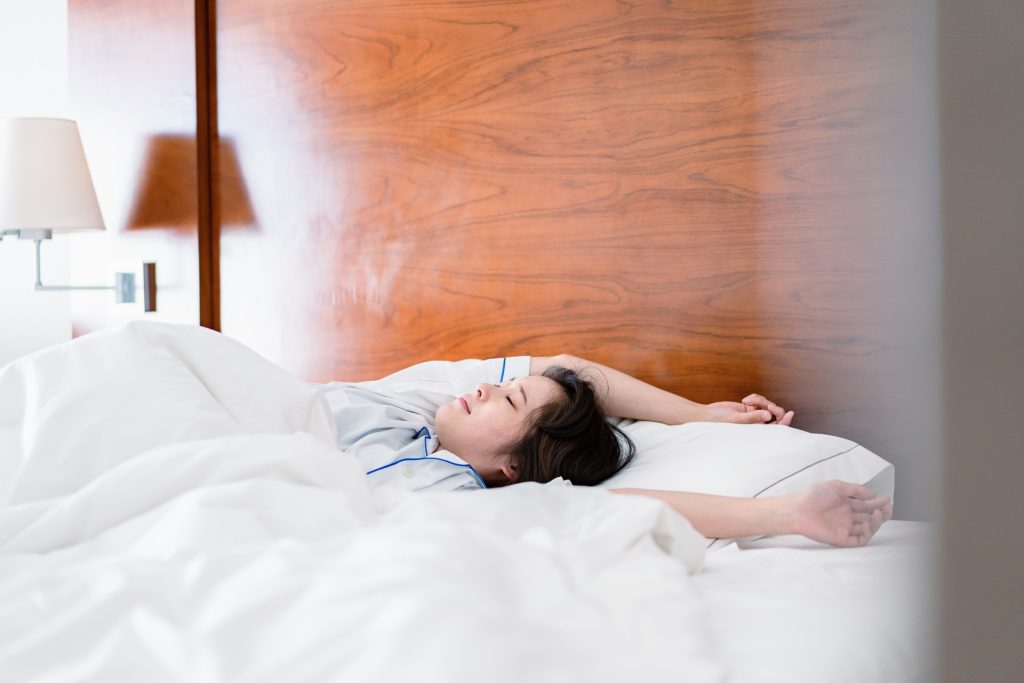 明るい時間にベッドで寝る若い女性