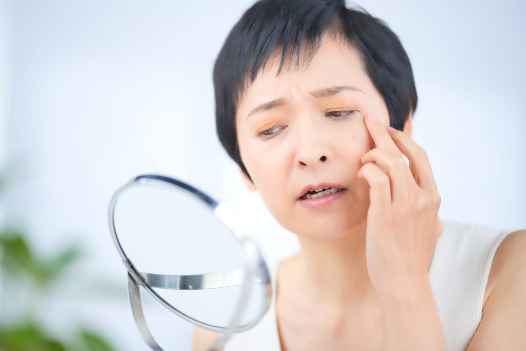 鏡を見て肌の目元を気にしているショートカットの女性