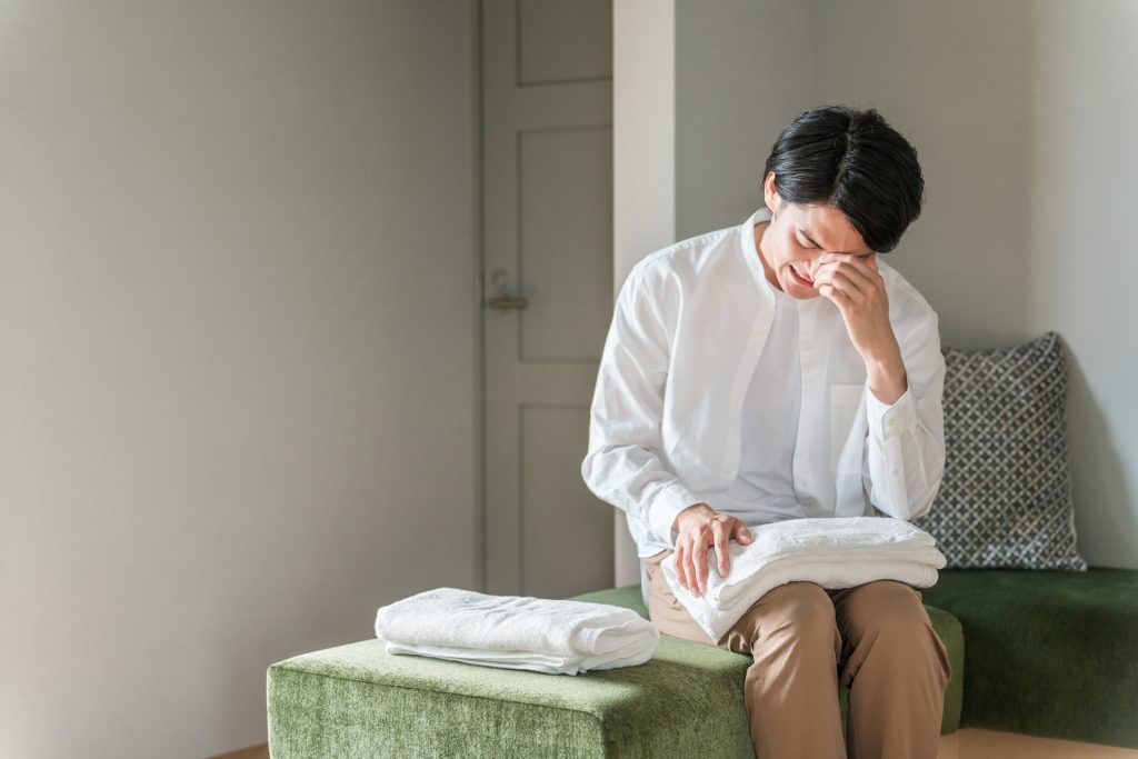 
自宅で洗濯物を畳みながら泣く男性（離婚）