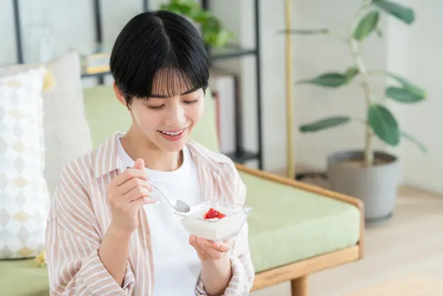 遺伝的背景や腸内環境を意識した減量中の女性が、低糖質・高たんぱく質のヨーグルトにイチゴを添えて摂取している様子。精密栄養(precision nutrition)や食事内容の個別最適化を視覚的に表現したイメージ。