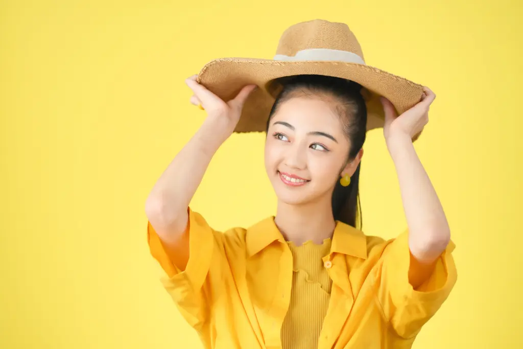 黄色背景で麦わら帽子をかぶる女性