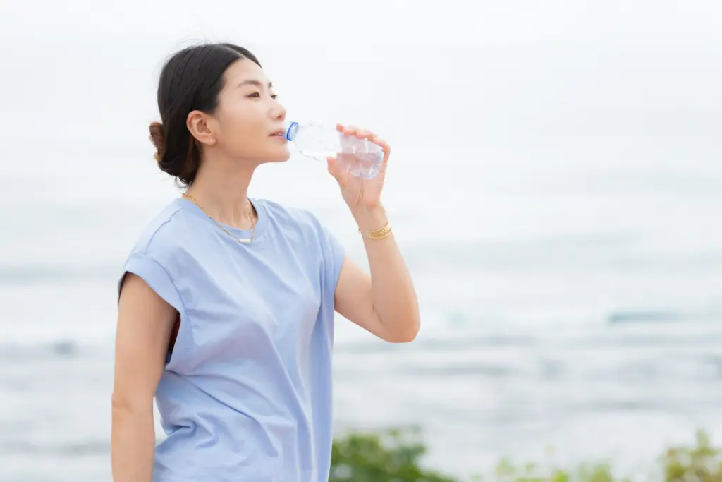 
海辺でペットボトルの水を飲む日本人女性