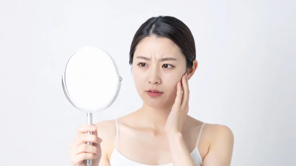 
鏡を見ながら肌の悩みを気にする女性