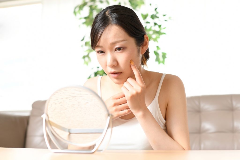 鏡を見ながら肌トラブルに悩む女性