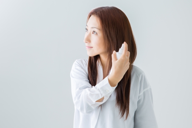 長く艶やかな髪の女性が、髪にミストを吹きかけながら遠くを見つめる。ヘアケア習慣を楽しんでいる様子が伝わる、美髪ケアや保湿ミスト使用の理想的なシーン。