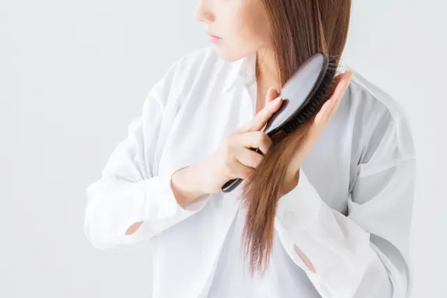 黒いヘアブラシで染めたダークブラウンの髪をとかす女性のイメージ。ブラッシングのたびに髪が抜ける様子を表現。人は年齢や人種に関わらず、生涯にわたり自然な脱毛を経験することを示すストック写真。