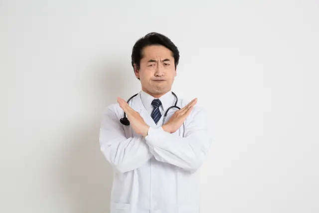 医師が腕をX字に交差させ、口を結んで厳しい表情を見せながら、はっきりと「NO(拒否)」を示している様子。若年男性への早期自毛植毛手術のリスク説明や、適切な治療方針の選択を促す場面を象徴するイメージ。