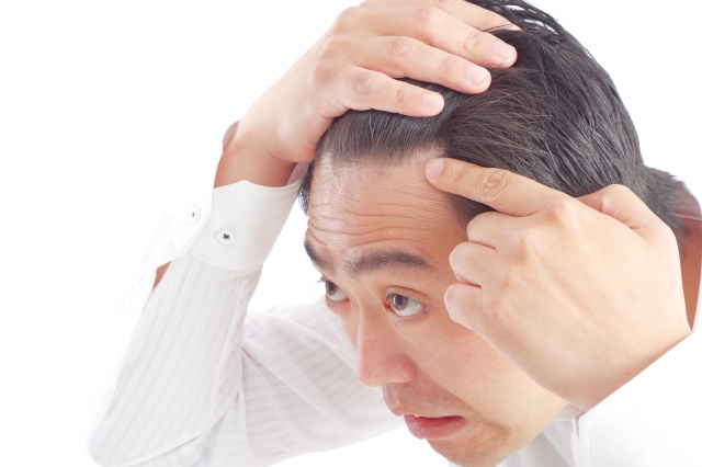 髪に手を当て、強い眼差しで前を見つめる男性。額には深いシワが寄り、薄毛や抜け毛への不安がにじむ表情。男性型脱毛症（AGA）に悩む様子を象徴するイメージ。