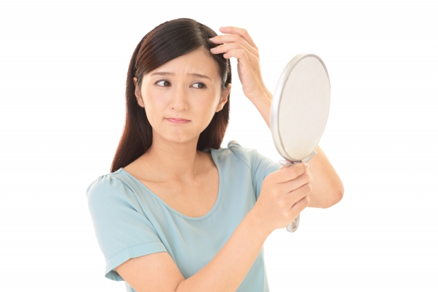 鏡の前で髪に手を添える女性。どこか不安げで自信をなくした表情が映し出され、鏡の中の自分も同じように頼りなく見つめ返します。髪や頭皮の悩みに心を奪われる瞬間。