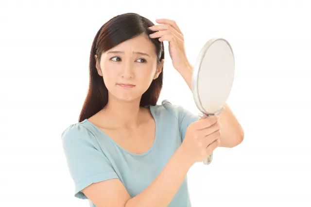 鏡の前で髪に手を添える女性。どこか不安げで自信をなくした表情が映し出され、鏡の中の自分も同じように頼りなく見つめ返します。髪や頭皮の悩みに心を奪われる瞬間。