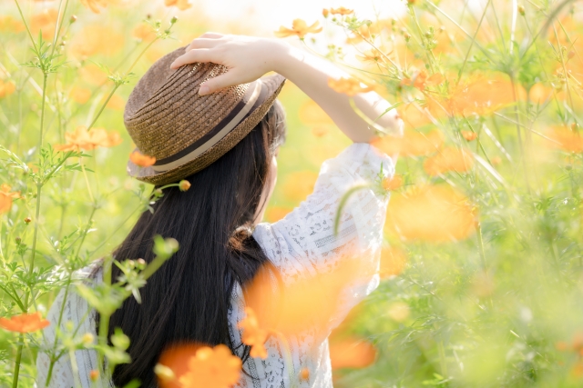 ヘア移植後の回復をサポートするPRP治療に関連するイメージとして、麦わら帽子をかぶった女性が美しいオレンジ色の花が咲いた道を歩くシーン。太陽の光が滑らかな肌とシルクのような黒髪を照らし、PRP治療による毛髪の健康や成長を象徴するかのように、自然な美しさが引き立っています。