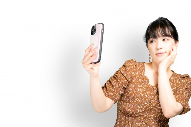 女性がスマートフォンを片手にポーズを取りながら体を傾けている様子。髪型や髪のボリュームが外見印象に与える影響と、他人からの印象が自己評価に及ぼす心理的な関係性を象徴するシーン。