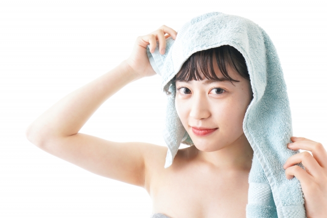 バスタイム直後の女性が、タオルを頭にのせたままカメラをまっすぐ見つめる。丸い瞳にほのかな笑み、赤い唇が印象的。ヘアケア後の満足感が伝わるリラックスした表情。髪と頭皮の美しさは、毎日の洗髪から。