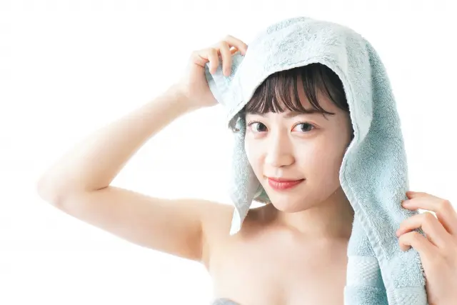 バスタイム直後の女性が、タオルを頭にのせたままカメラをまっすぐ見つめる。丸い瞳にほのかな笑み、赤い唇が印象的。ヘアケア後の満足感が伝わるリラックスした表情。髪と頭皮の美しさは、毎日の洗髪から。