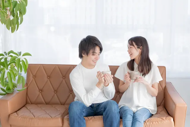 明るいリビングで、男性と女性がソファに並んで座り、ティーカップを手に笑顔で会話を交わす様子。将来のヘアケアや薄毛治療について前向きに語り合うような、希望に満ちた雰囲気のイメージ。