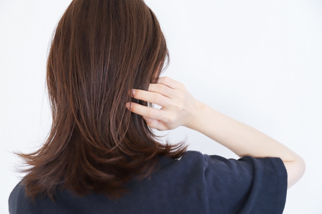 「髪の移植を考える際、後頭部の毛髪が手で移動され、肩周りで整然とカールした暗い茶色の髪と白い肌が鮮明に対比されています。後頭部はドナー部位としてよく使用され、髪を採取する際に重要なポイントとなります。