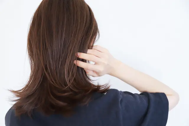 「髪の移植を考える際、後頭部の毛髪が手で移動され、肩周りで整然とカールした暗い茶色の髪と白い肌が鮮明に対比されています。後頭部はドナー部位としてよく使用され、髪を採取する際に重要なポイントとなります。