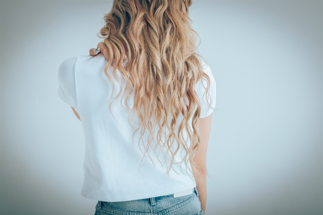 金色に輝くなめらかな髪が女性の華奢な背中に沿って優雅に波打つ様子。最高級の糸のように柔らかくカールしながら光をまとって流れ落ちる、美しく健康的なドナーヘアの象徴的イメージ