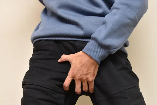 片手は頭に、もう一方の手は血管が浮き出るほど力強く股間を押さえる男性。言葉は発せられなくとも、その苦痛の深さは一目で伝わってきます――前立腺の異常や疾患の可能性を、身体は沈黙のうちに訴えているのかもしれません。