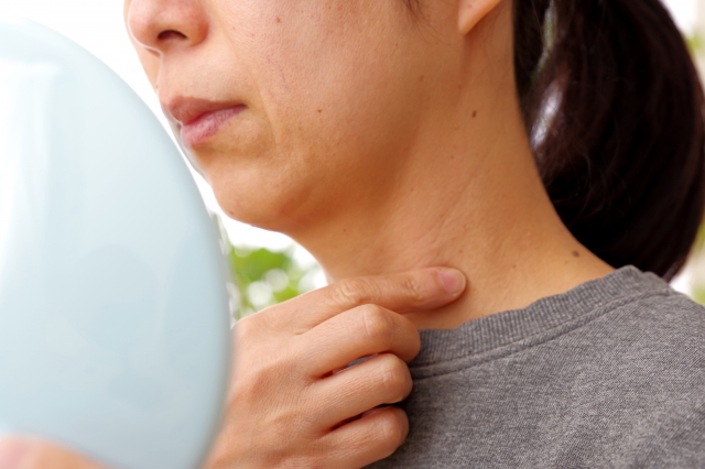 手鏡を見ながら首元のたるみを気にする中年女性の口元から首にかけての様子