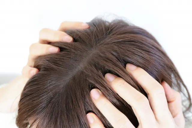 こめかみに置かれた両手が、指先で髪をかき分けながら頭皮に触れている様子。頭皮は繊細かつ複雑な環境であり、植毛治療の前後を通じて丁寧なケアと十分な配慮が必要であることを象徴するイメージ。
