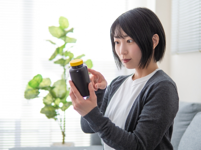 サプリメントのボトルラベルを指でなぞりながら、その健康効果を期待するように見つめる女性の様子。健康食品や栄養補助サプリの使用とイメージに関するビジュアル。