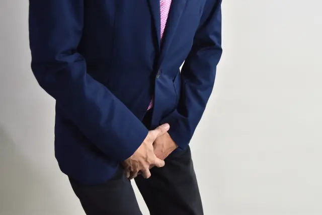 スーツ姿の男性が下腹部を押さえ、強い痛みに顔をゆがめながら前かがみに。前立腺がんと診断されたが、その原因がまさか薄毛治療薬だったとは――頭髪と前立腺、無関係に思えるこのふたつの領域に、思いがけない関連があるのかもしれません。