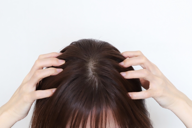 女性が頭皮をマッサージしている様子。写っているのは指先と頭頂部のみだが、健康な髪を育むためには、髪の表面だけでなく、頭皮と毛根にまで意図的なケアが必要であることを示唆している。