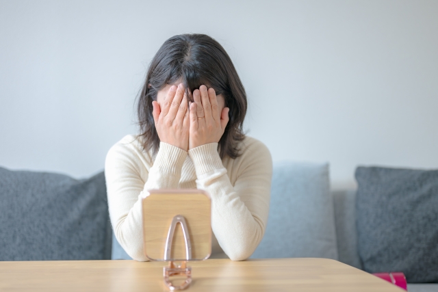鏡の前で顔を手で覆い、深く落ち込む若い女性。かつての豊かな髪が失われつつある現実を直視できず、同世代よりも早く始まった薄毛の進行に強いショックと不安を感じている様子。女性の脱毛症や若年性の薄毛に悩む姿を象徴的に表現したイメージ。