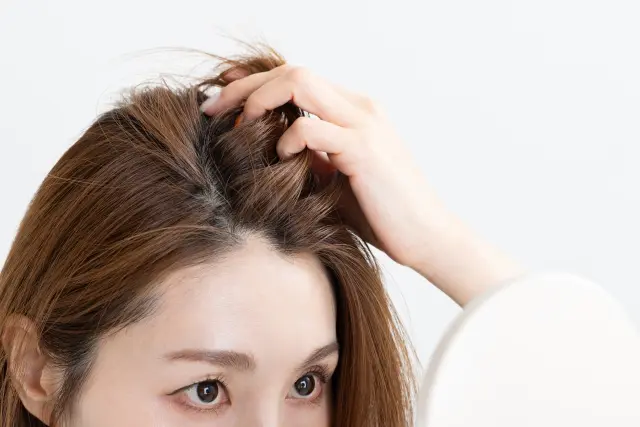 鏡越しに頭皮を見つめる女性。髪をかき上げ、薄くなった分け目や地肌を真剣に確認している。薄毛の悩みは深刻だが、「きっと何か方法がある」と希望を捨てずに向き合う姿。薄毛対策や毛髪再生に関心のある女性に共感を呼ぶ一枚。