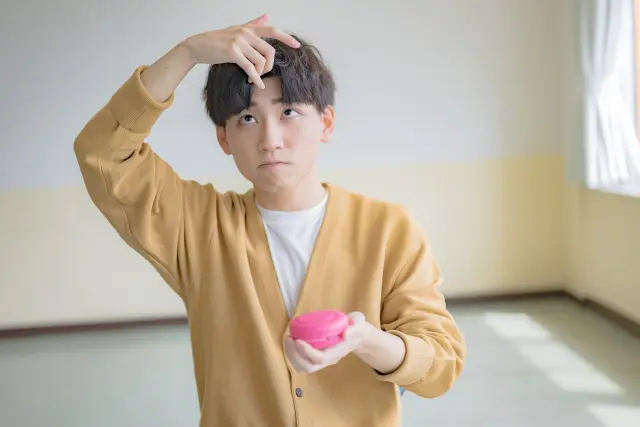 ヘアワックスを使って髪型を整える若い日本人男性。自宅でのヘアスタイリングや薄毛対策後のヘアセットをイメージさせる日常シーン。