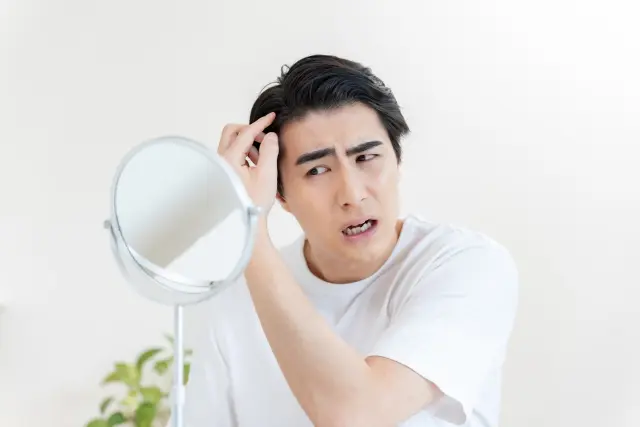 鏡を見つめ、口を開けたまま深い不安の表情を浮かべる中年男性。進行する薄毛に戸惑い、現実を受け入れられず苦悩する様子