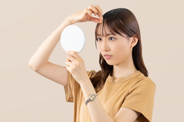 毛髪再生手術後、自分の髪に自信を持ち、手鏡を使って前髪を慎重に整える女性のシーン。髪は背中や肩を流れ、胸元に届く直前で美しく整えられています。彼女はその仕上がりに満足している様子です。