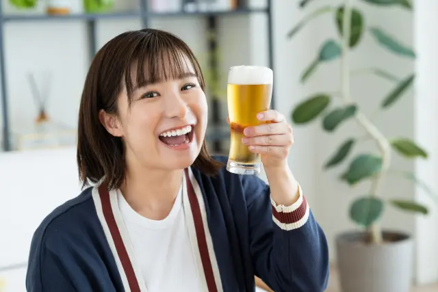 夜にビールを楽しむ女性の笑顔|飲酒習慣が知らず知らずのうちに引き起こす肌荒れリスク|毎晩の晩酌と美容トラブルの関係に注意喚起するイメージ写真