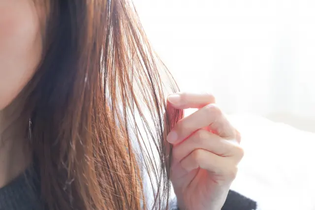 女性の顔は頬から外側だけが見え、透けるような手が乾燥した茶色に染められた髪の毛を感じている。その髪は輝きを失い、ツヤがなくなっている。髪を切ったり、ダメージを受けたりしても、血が流れることも痛みを感じることもないが、それでも髪は私たちの一部である。