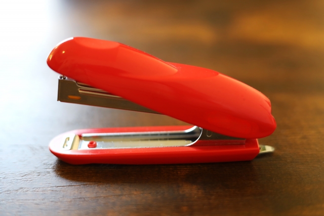 トマトレッドカラーのホッチキス（ステープラー）のクローズアップ画像。自毛植毛手術で使用されるパンチ機器の形状が一般的なホッチキスに似ていることから、その比較対象として用いられるイメージ写真