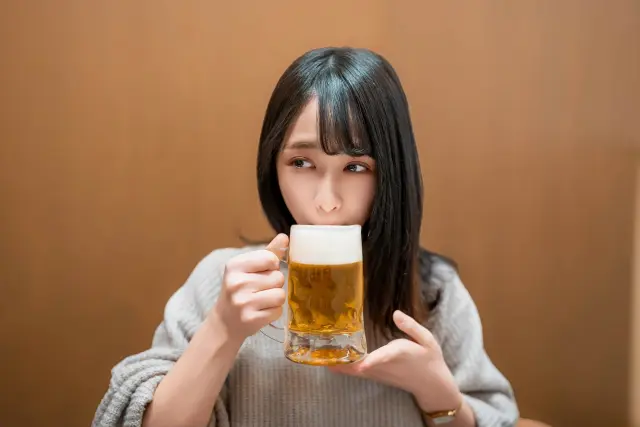 大きめのビールグラスからビールを口にする女性の姿。飲酒習慣やアルコール摂取と健康・美容への影響を象徴するイメージ。