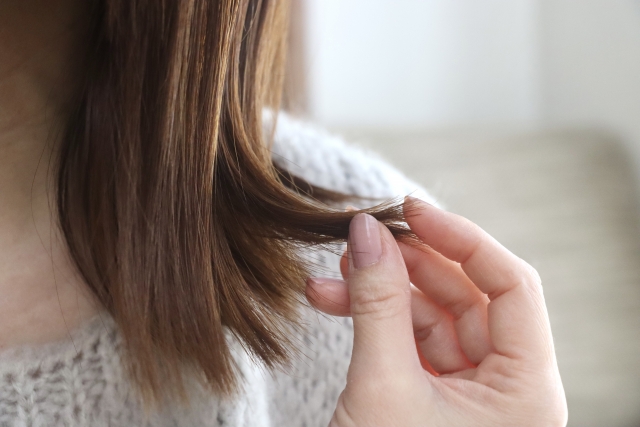 茶色の髪先にそっと触れる女性。薄毛治療を検討中でしょうか？髪は「女性の命」とも言われる大切な存在。治療を考える前に知っておきたいポイントがたくさんあります。#薄毛治療 #ヘアリストレーション #女性の髪悩み