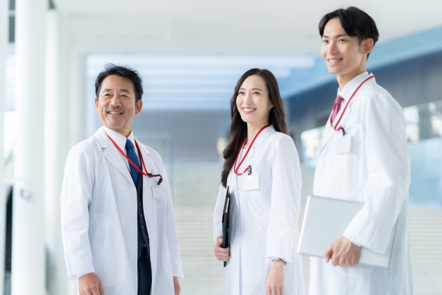 白い柱が並ぶ廊下で笑顔を見せる2人の男性医師と1人の女性医師。純白の白衣に身を包み、髪に悩む患者たちの未来を見据えるように揃って横を見つめる姿は、毛髪再生医療への確かな信念と希望を象徴している。科学の力で、薄毛に悩む男性を再びたてがみのあるライオンのように、髪を失った女性を再び笑顔に導くという想いを込めたイメージ。