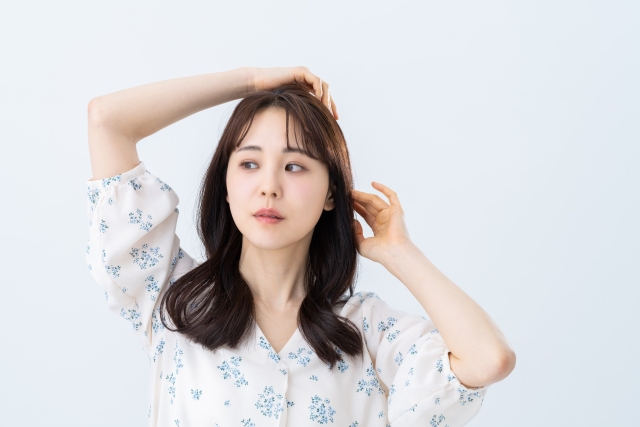 両腕を上げて髪にそっと触れる若い女性。小さな青い花柄が散りばめられた白いブラウスが、肩に沿ってなめらかに流れる豊かな黒髪を引き立てます。自然な仕草と艶やかな髪の美しさが際立つ、女性らしさ溢れる瞬間。