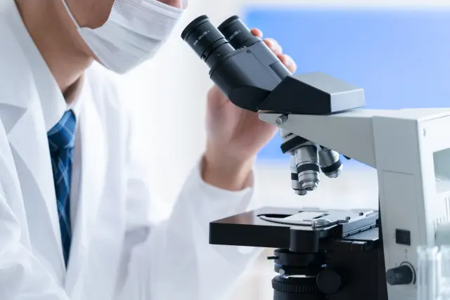 白衣を着た研究者が、顕微鏡の接眼レンズを調整している様子。毛髪や毛包の微細構造を観察する準備をしている場面。