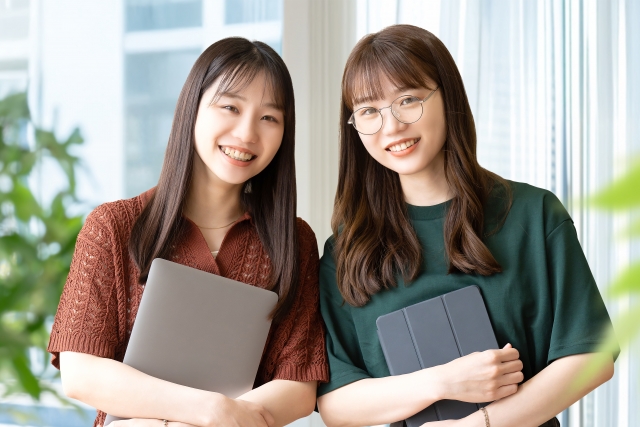 ウェーブヘアの女性と直毛の女性が並んでカメラを見つめる姿。髪の形状の違いが外見に与える印象を象徴するイメージ。