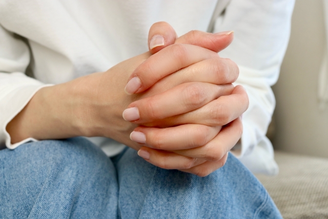 膝の上にそっと重ねられた細く繊細な両手。控えめな仕草が、外見の変化を前にした静かな決意や、薄毛治療への期待と不安を内に秘めた心情を静かに表現しているワンシーン。