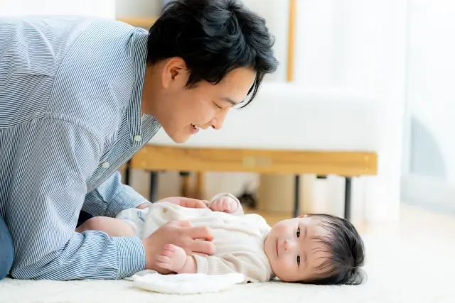 床に敷いたマットの上で、父親が赤ちゃんの息子と楽しそうに遊ぶ姿。遺伝によって受け継がれる特徴が、将来、目に見えるかたちで現れることを示唆する場面。薄毛の傾向も遺伝的に受け継がれる場合があり、望むものも望まないものも受け継ぐのが自然の摂理であることを表現している。