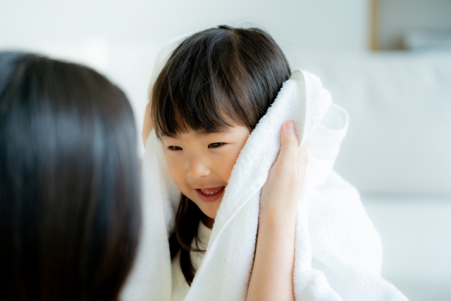 ふわふわのタオルで優しく髪を乾かすお母さんに、笑顔を見せる小さな女の子。光にやわらかく輝く黒髪が美しく、髪が私たちと共に育っていくことの素晴らしさを感じさせます。髪の成長、毛包、親子のふれあいが伝わる一枚。